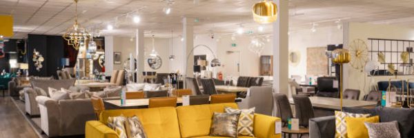 A wide angle of a furniture store with no people in. There is various different sofas and lamps and furniture on the shop floor for display purposes.