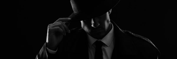 Old fashioned detective in hat on dark background, black and white effect