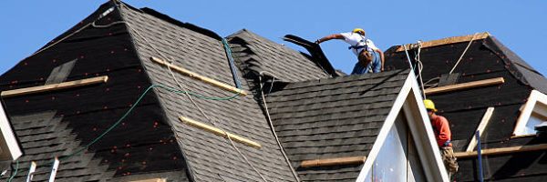 Construction workers putting shingles on the roof of a house.